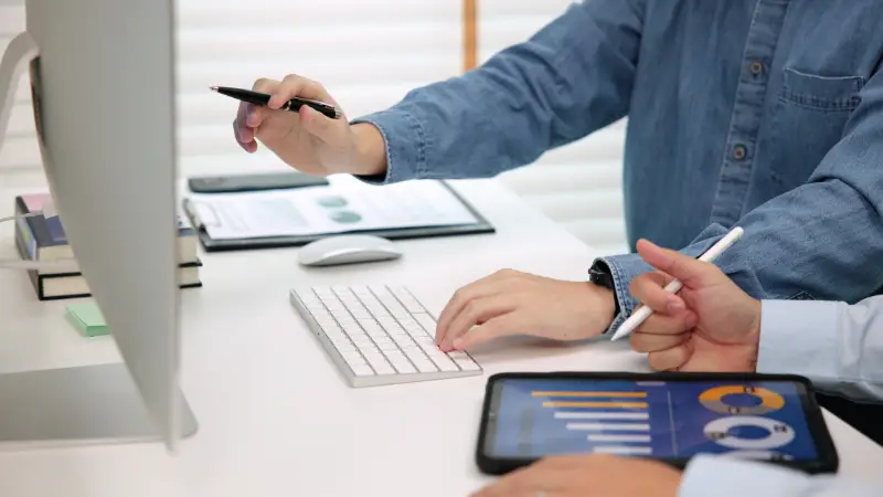 Two professionals reviewing charts on a tablet and computer