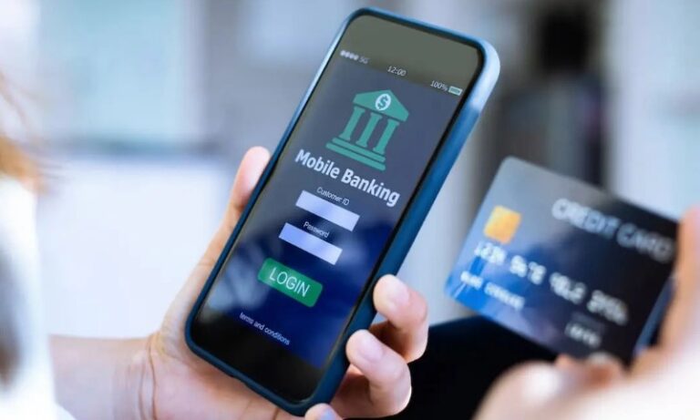 A person holds a smartphone with a mobile banking login screen and a credit card